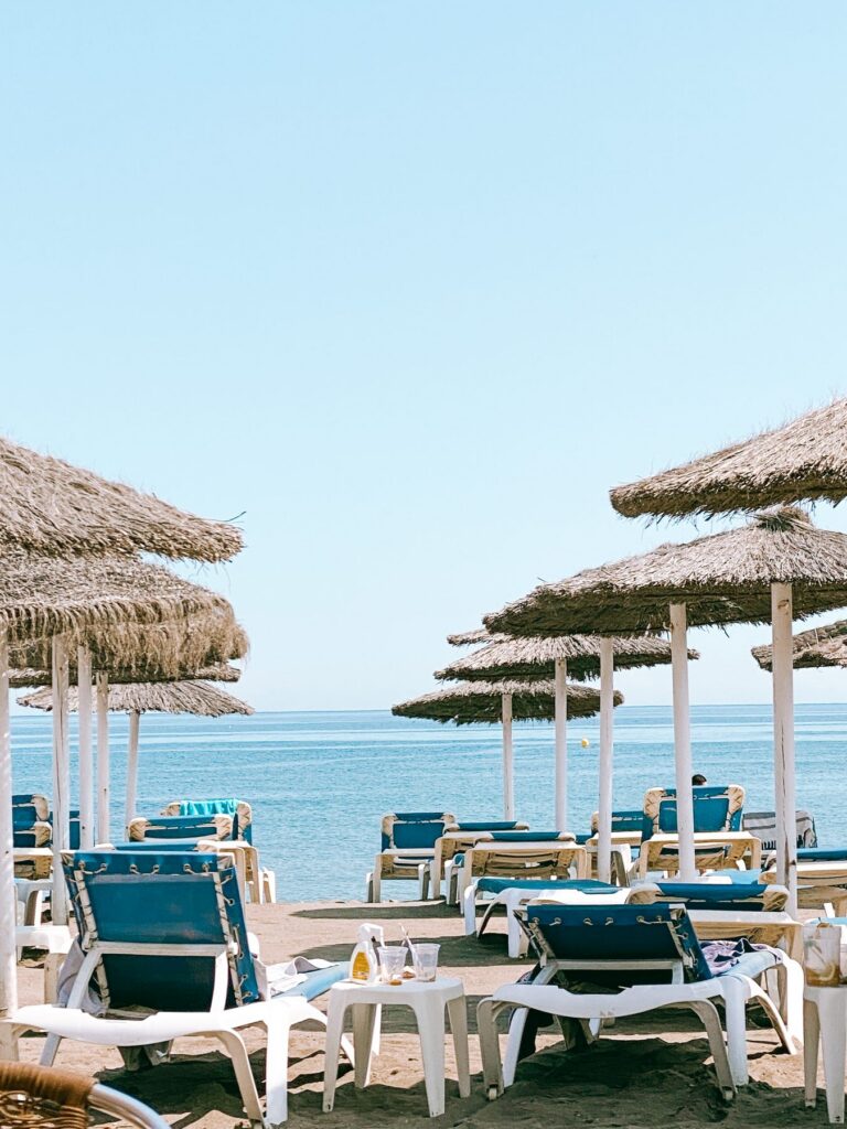Thatched parasols and sun loungers on an Estepona beach facing a flat, clear Mediterranean