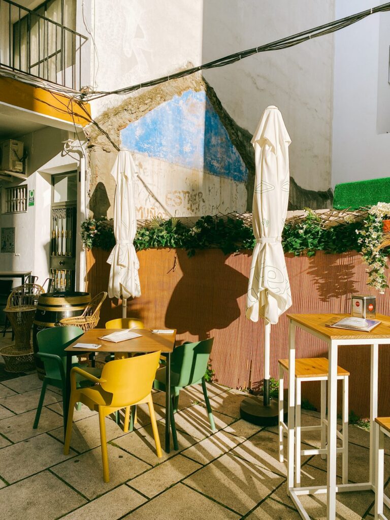 Yellow and green chairs on a small street terrace in Estepona old town, with parasols and late afternoon shadows across the paving